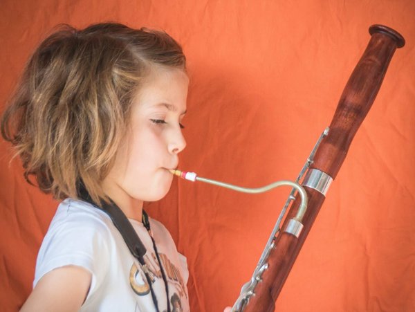 Vor einem orangefarbenen Hintergrund spielt ein Mädchen das Instrument Fagott.