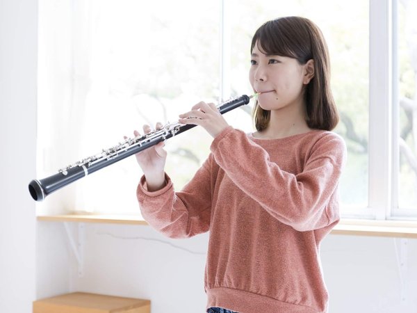 Ein Mädchen steht vor einem Fenster und spielt das Instrument Oboe.