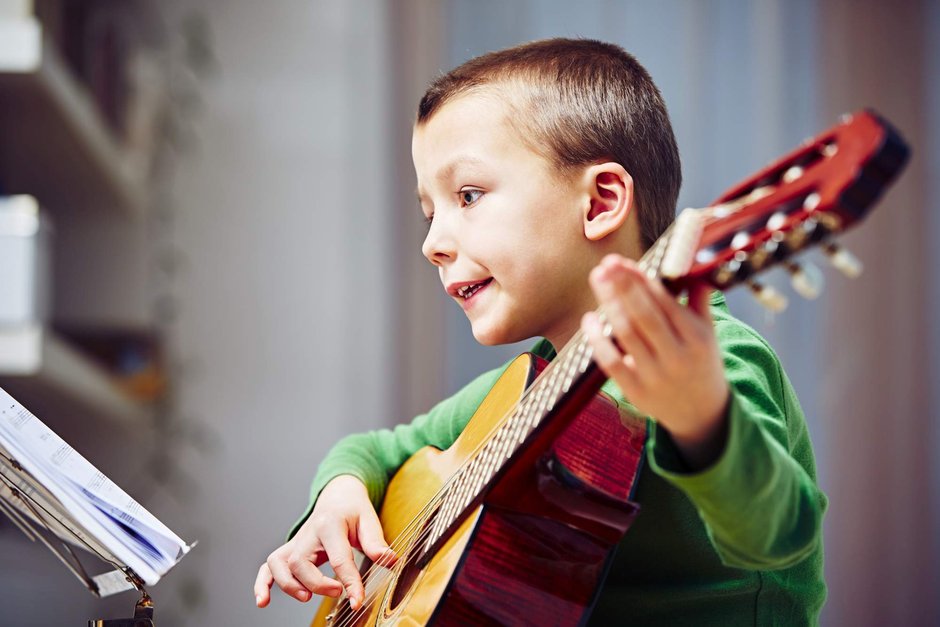 Ein kleiner Junge sitzt vor einem Notenständer und spielt auf der Gitarre.
