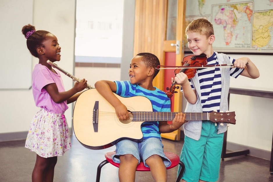 Drei lachenende Kinder spielen die Instrumente Gitarre, Querflöte und Violine